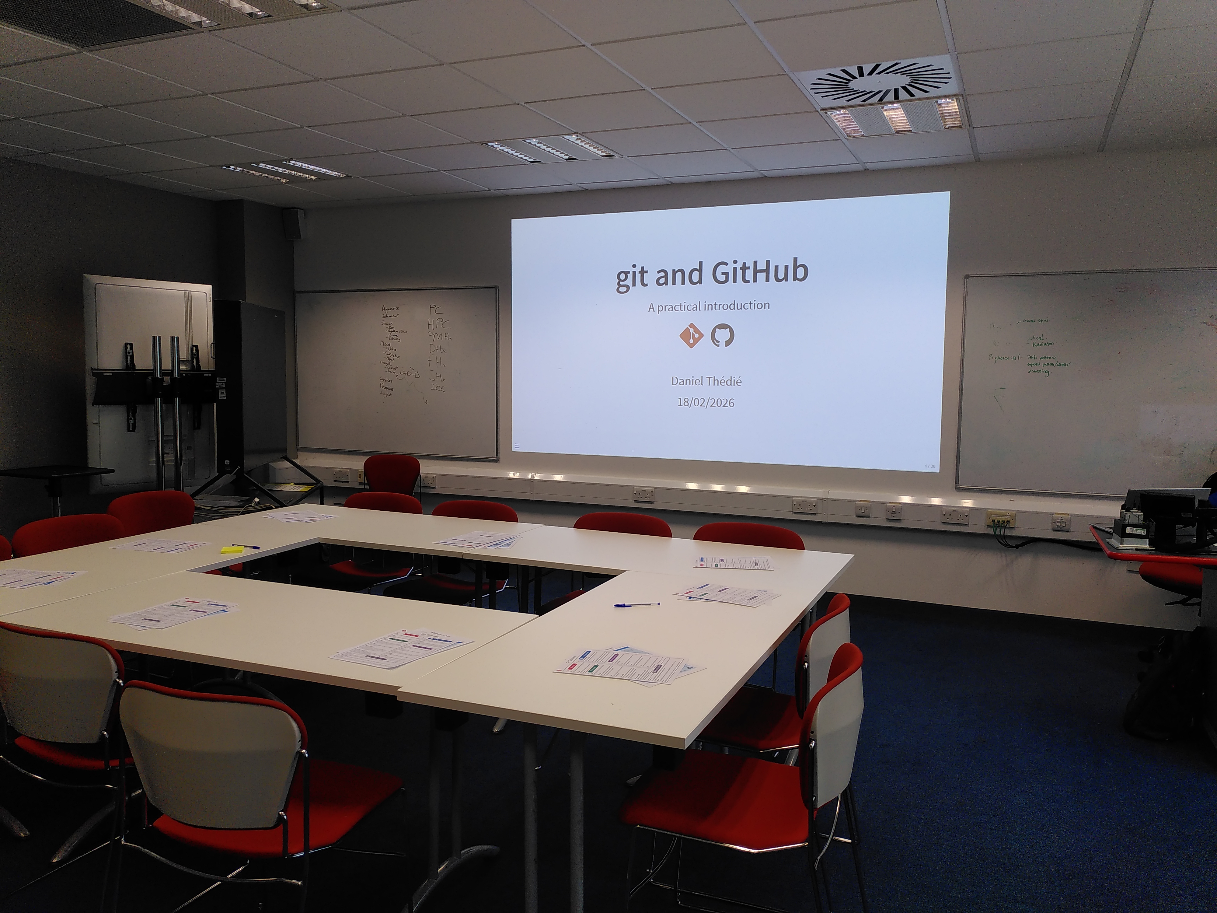 the room for the git workshop. A title slide is projected, and sheets of paper are on the tables